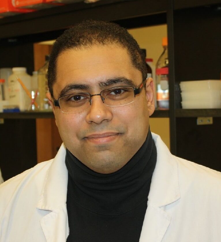 Professional headshot of Bilal Qizilbash, CEO of EK Foods, wearing a lab coat and a friendly smile in a laboratory.