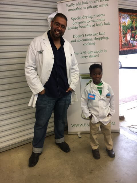 Bilal Qizilbash, scientist, and a little kid, both wearing lab coats, strike a cool pose with hands in their pockets.