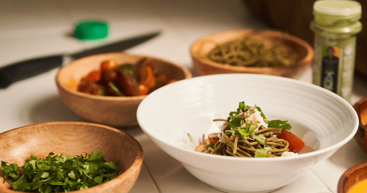 A flavorful combination of Bilal's EasyKale powder sprinkled on a fresh tomato salad and a serving of Raan Raan Italian pasta, garnished with parsley, presented in a wooden bowl.