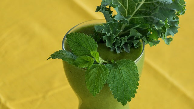 Invigorating green vegan smoothie with fresh organic kale leaves and aromatic lemon balm on a vibrant yellow background.