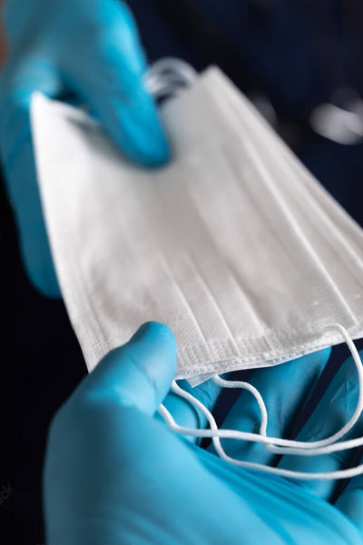 Close-up of hands wearing medical gloves exchanging face masks, highlighting the proper hygiene practices and the exchange of protective equipment.