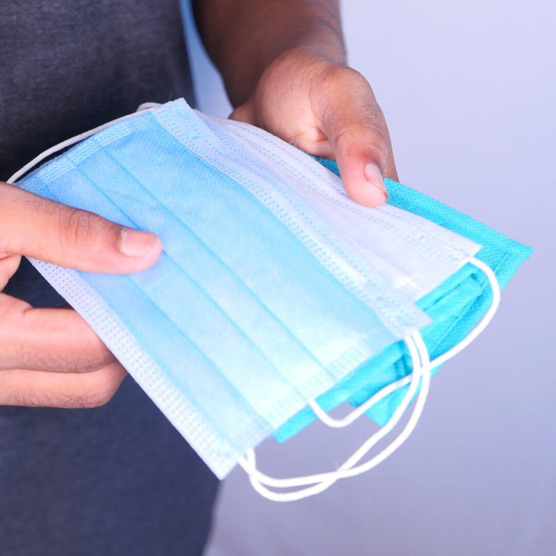 Close-up of hands holding a protective face mask, emphasizing its role in preventing the spread of COVID-19 and promoting public health.