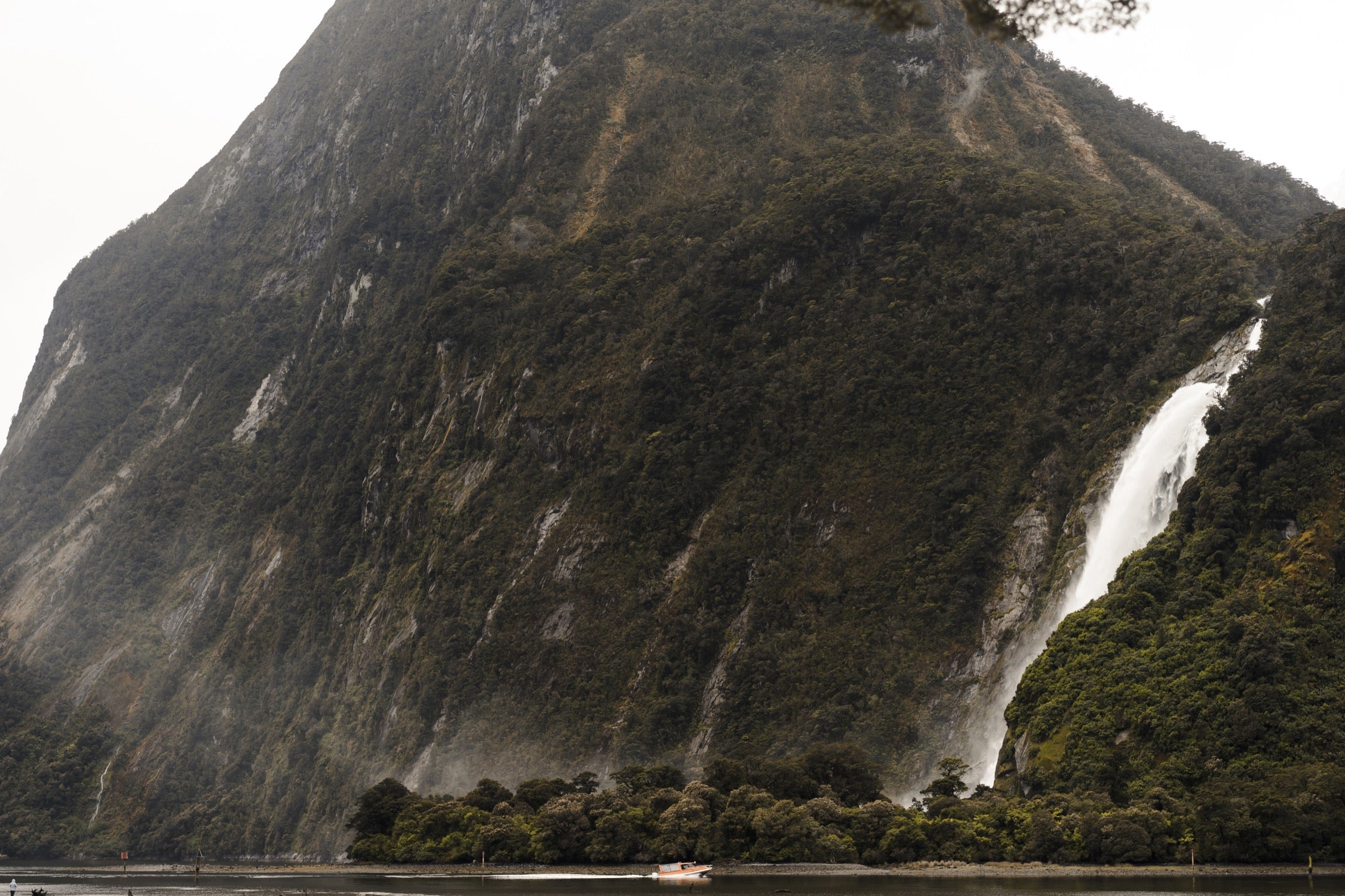The Milford Sound waterfall. A small motorboat passes by in the water below.