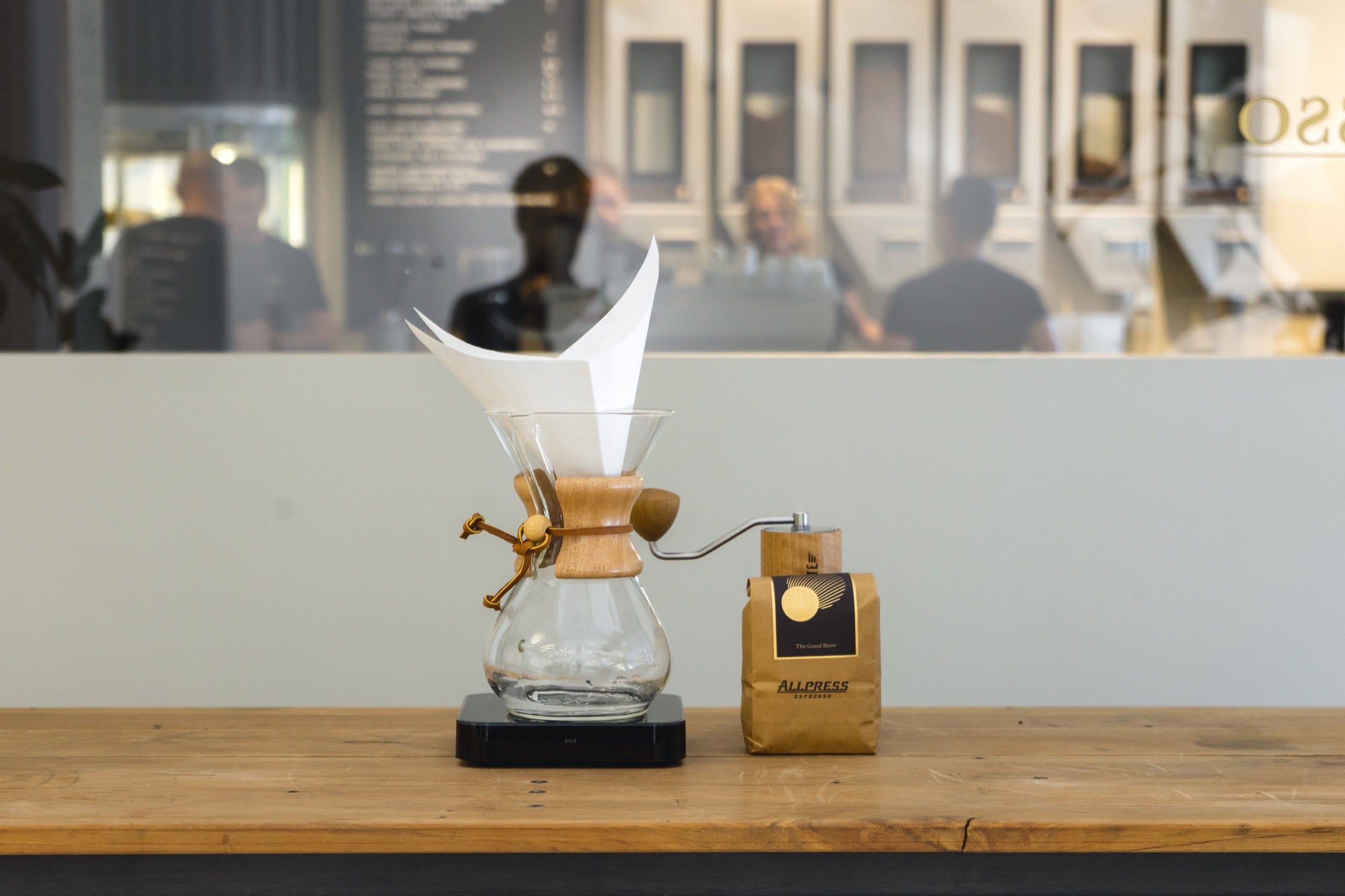 A Chemex pour-over on a set of scales, next to a bag of coffee and a grinder