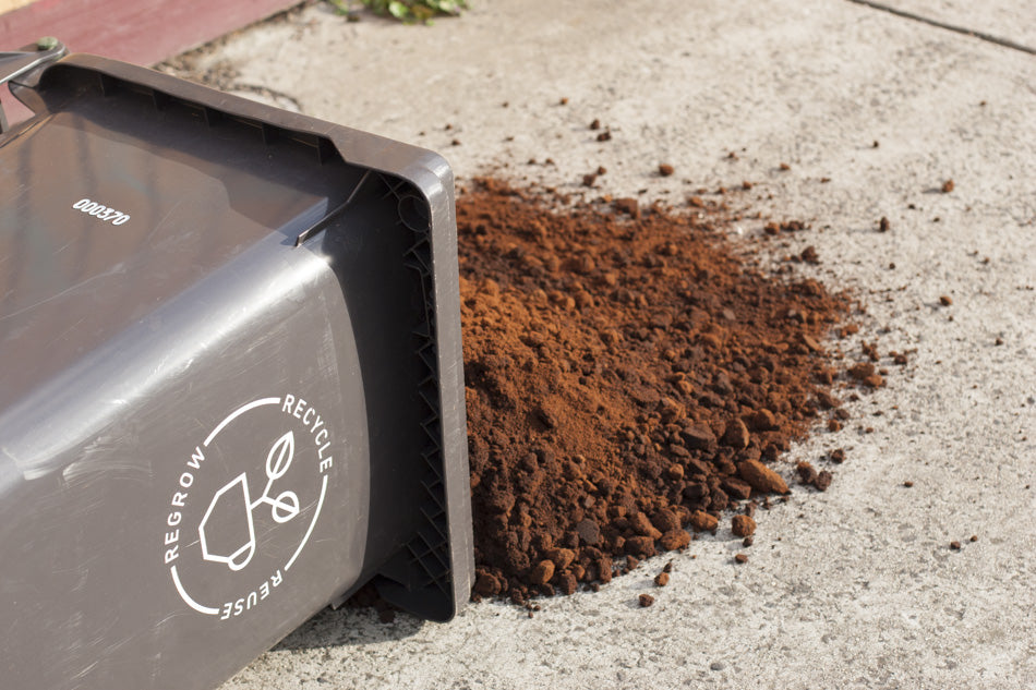 Coffee grounds spilling from a Reground recycling bin bearing the motto 'Recycle, Reuse, Regrow'.