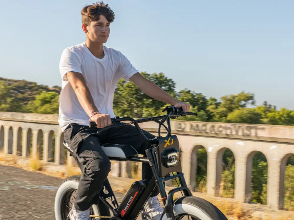 Macfox X1S electric bike being ridden along a scenic stone bridge on a sunny day