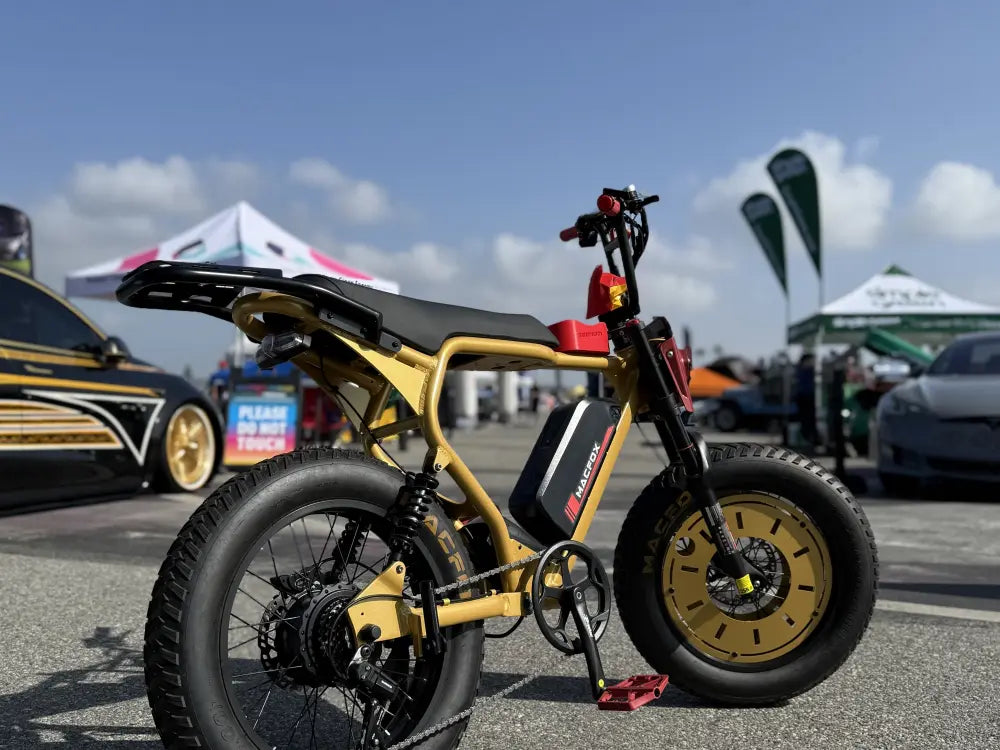 Macfox X2 electric bike displayed in a parking lot with custom gold styling and a row of cars behind it