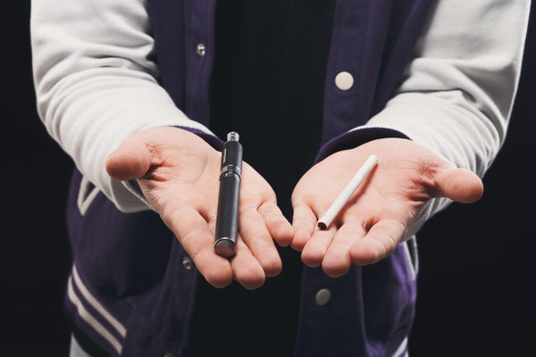 A boy is holding both a vaping device and cigarettes.