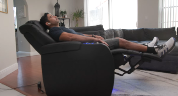 Person reclining in a black leather electric home theater sofa with their feet up, showing the fully extended footrest