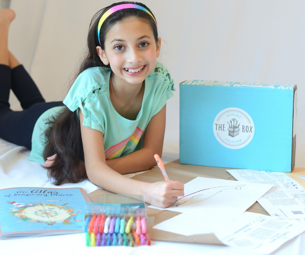 An elementary school-aged girl with long dark hair and a rainbow headband lays on the floor and colors a picture with gel pens that she got from her Outside The Box Creation subscription box.