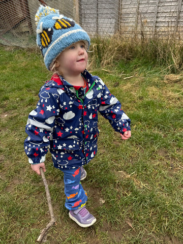 Image of a toddler wearing blue jogging bottoms, a coat and a winter hat holding a stick.