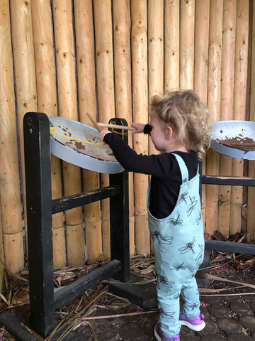 Toddler playing the steel drums wearing a black long sleeved tshirt and some damselfly dungarees