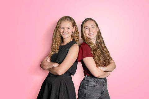 Co-Founders Emily and Riley pose back to back with arms crossed in front of a pink background. They look like badass business owners.