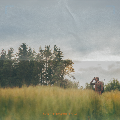 A photo of a hunter in a field with binoculars. He is glassing looking for wild game. Trees are in the background behind the hunter.