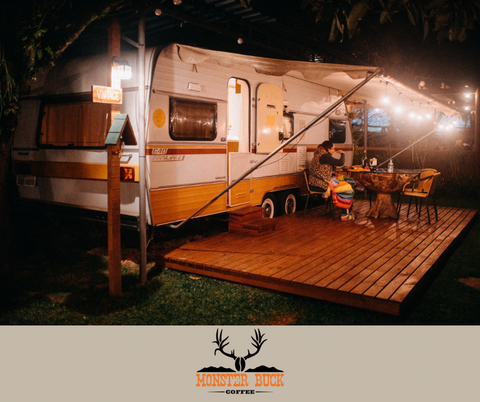 A camper set up camp in the Forrest with an awning full of lights and a picnic table.
