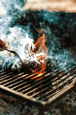 Wild game meat on a grill with smoke and fire around it.