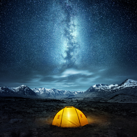 A yellow tent light up at night with the night sky lit up by stars and the Milky Way.