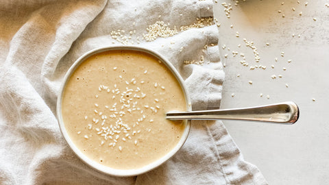 Creamy tahini paste in a bowl, a spoon adorned with sesame seeds nearby—inviting you to indulge in the nutty richness of this versatile ingredient.