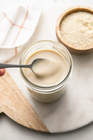 ndulge in creamy tahini straight from the jar against a backdrop of scattered sesame seeds.