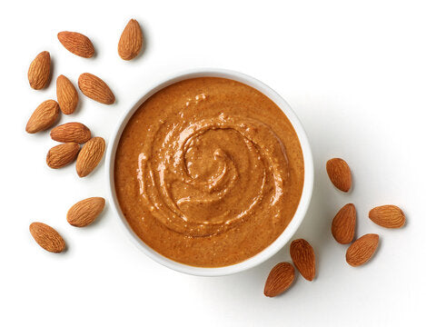 A luscious bowl of almond butter takes center stage, surrounded by scattered almond pieces, offering a tantalizing glimpse into the delicious world of almonds.