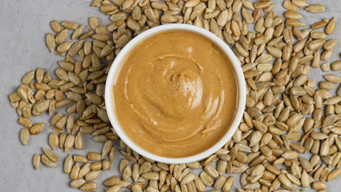 An inviting scene unfolds: a bowl filled with wholesome sunflower seeds sits beside a jar of creamy sunflower butter, promising a delectable journey through nutty flavors and nourishing indulgence.