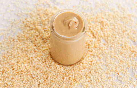 Sesame paste in a jar surrounded by sesame seeds.