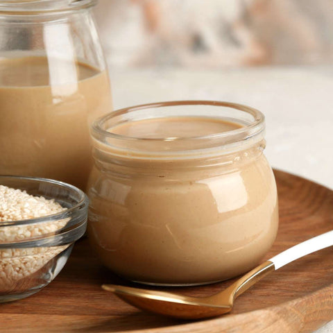 Tahini sauce in two jars with sesame seeds in a bowl.