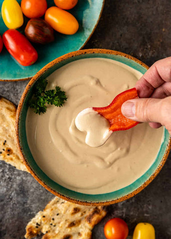 Delight in a bowl of velvety tahini, perfect for dipping with crisp vegetables and warm pita, adorned with a fresh sprinkle of parsley for a burst of flavor.