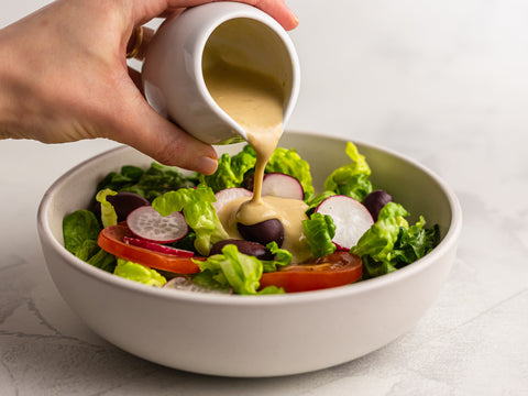 A salad bowl with lettuce, tomatoes, beets, olives, and Tahini dressing.