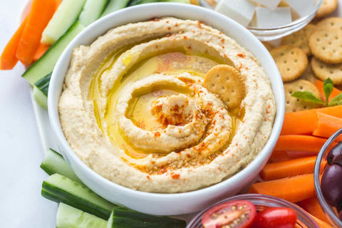 Hummus, the star of the spread, is surrounded by an array of colorful sliced vegetables and crisp biscuits, inviting you to dip, savor, and enjoy a harmonious medley of flavors and textures.