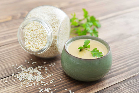 Tahini sauce in a bowl, garnished with parsley, beside a jar of sesame seeds.