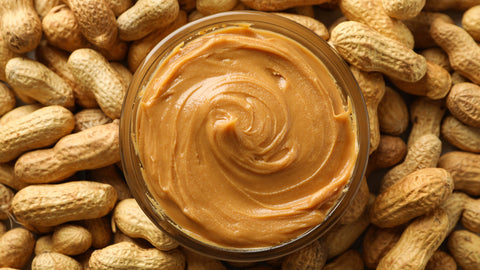 A tempting sight: a bowl overflowing with creamy peanut butter rests atop a bed of whole peanuts, inviting you to savor the rich, nutty goodness within.