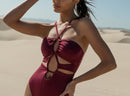 Model wearing maroon strappy halter one piece with cutout design in the desert.