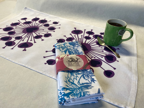 handprinted kitchen towel flat on table with cup of tea and a pair of kitchen towels with decorative paper band
