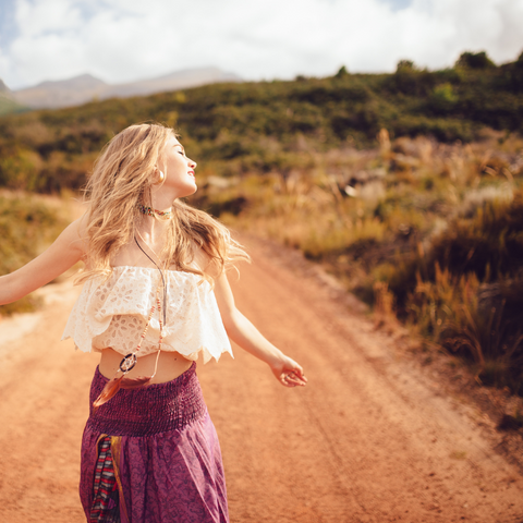 Boho Beach girl walking down a dirt path, flowing skirt, and white top, arms outstretched