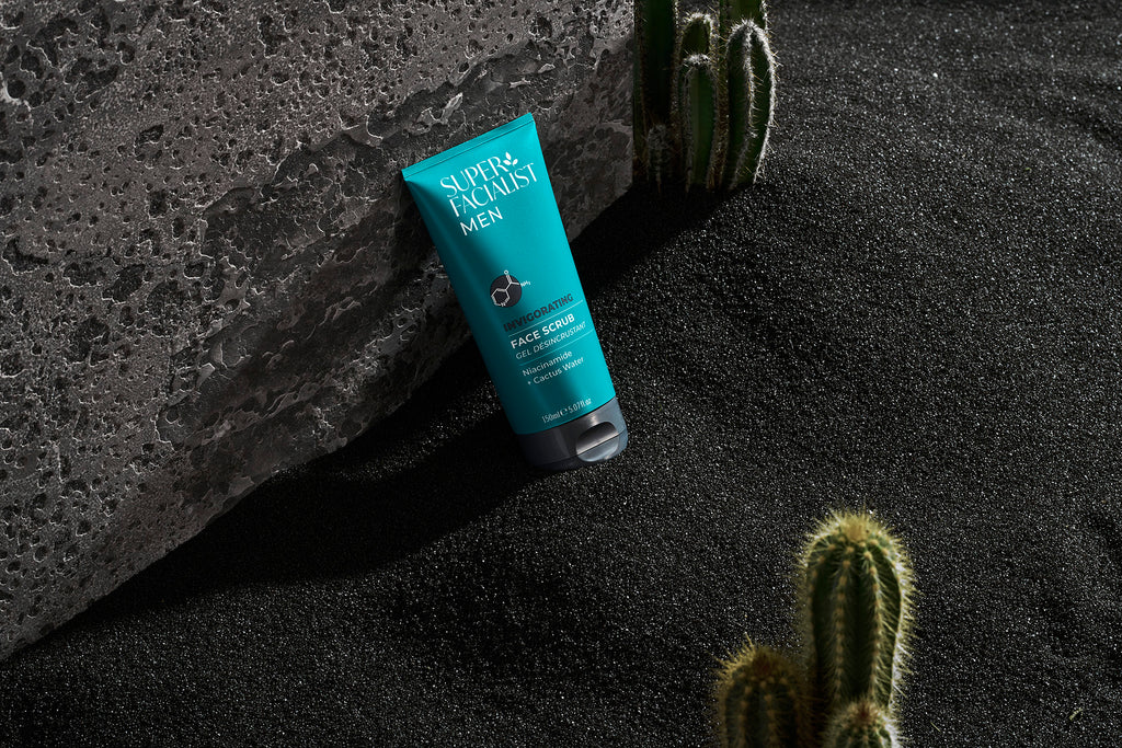 face scrub in black volcanic sand leaning against grey stone away with cactuses around skincare for men