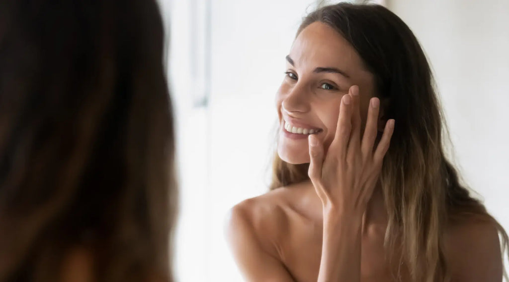 woman touching her skin while looking in the mirror