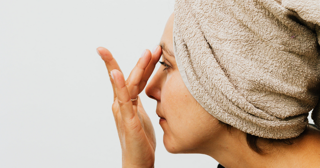 woman with hair towel applying eye cream