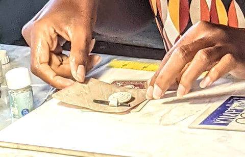 A pair of hands are seen working on a piece of metal clay jewelry.