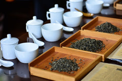 Image of white tea tasting sets with trays of looseleaf tea in front of them.