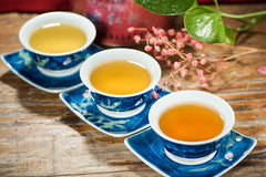 Three cups of different colored teas served in blue/white Asian looking cups/saucers setting on a wooden table.