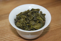White tea cup without handle filled with green brewed tea leaves