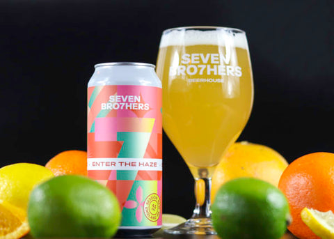 A can of Enter The Haze with a glass poured surrounded by fruit.