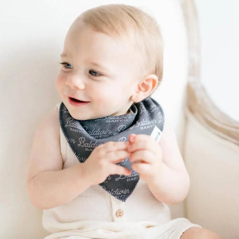 Baby boy wearing charcoal gray bib with Baldwin Baby Co logo printed on it in a lighter gray