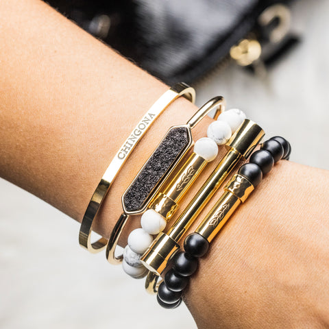 Hispanic woman's wrist featuring five different bracelets. one of the bracelets is a Gold-plated stainless steel cuff bracelet with the word 'Chingona' stamped into it.  bracelet for Spanish speakers
