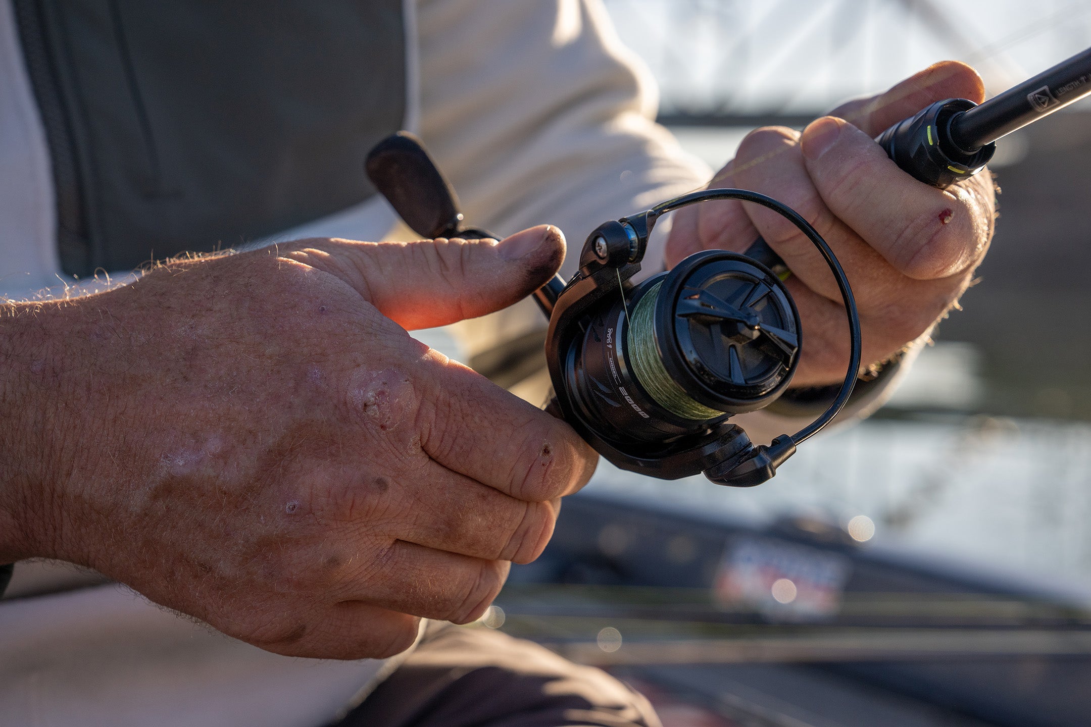 Hands holding a spinning reel while fishing.