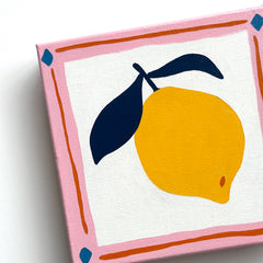 canvas oil painting of a bright yellow lemon with navy blue leaves and a pink and orange border