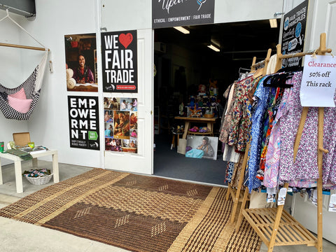 The entrance to a bright Fair Trade shop with a specials rack out the front and a cool chair hammock hanging