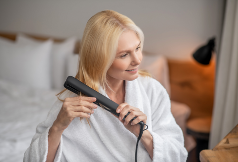 mature blond woman using flat iron on her hair