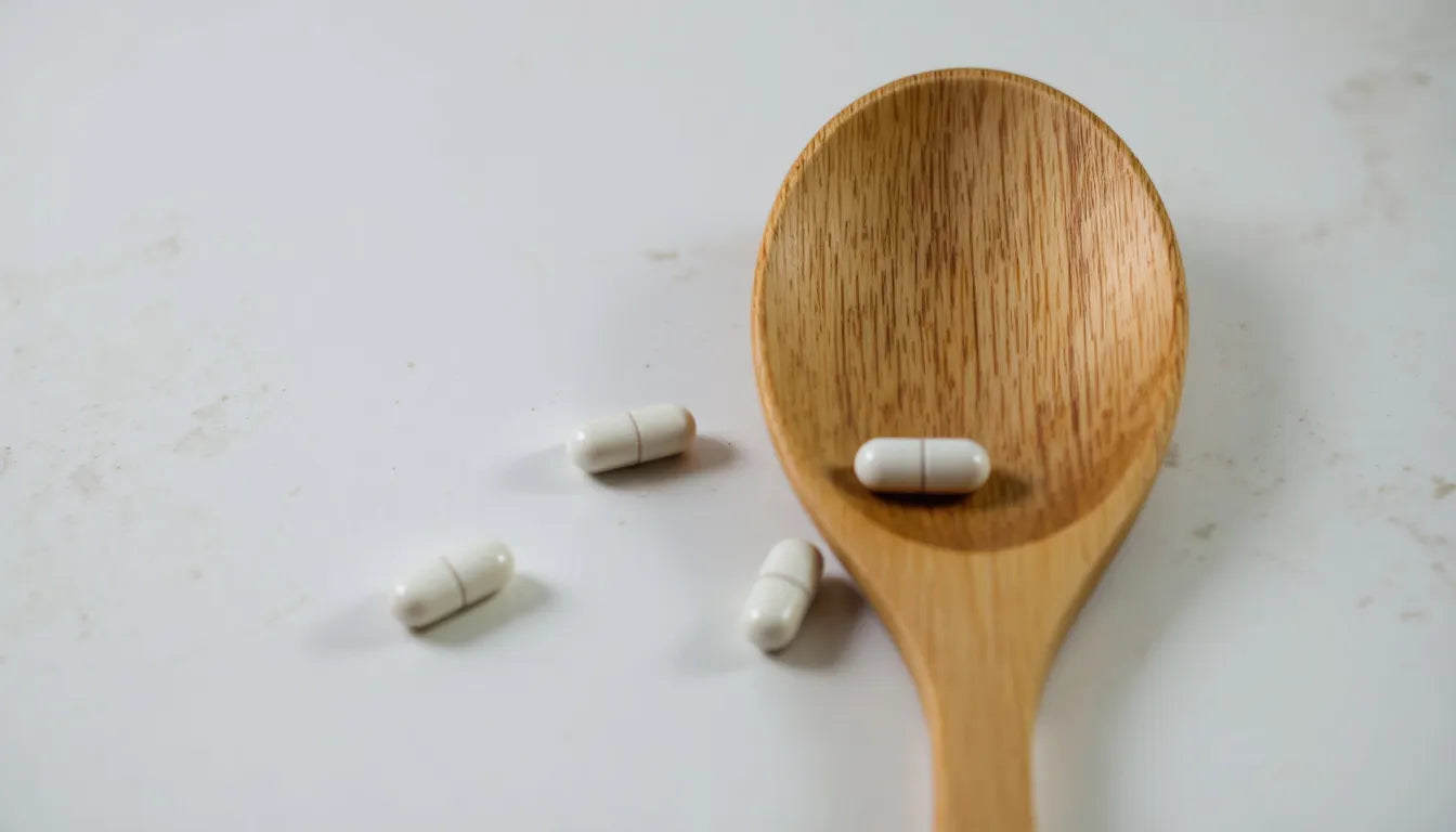 White supplement capsules resting on a wooden spoon.